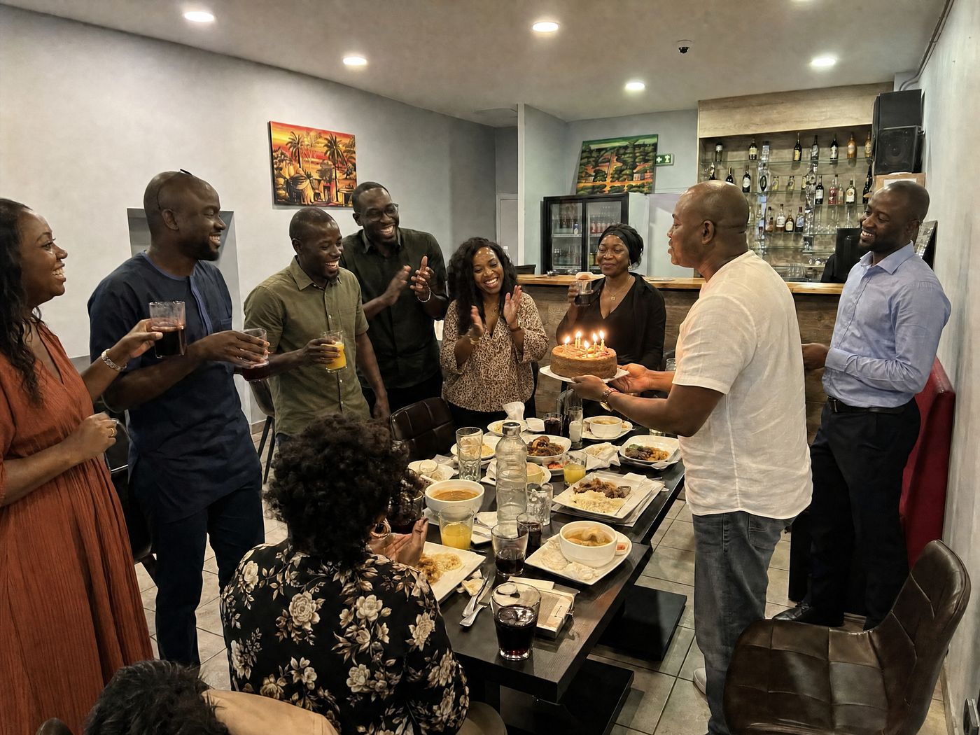 Photo d'un anniversaire dans la salle du restaurant africain Sepela, un gâteau aux bougies et les invités debout autour de la table, repas de groupe à Lyon 7