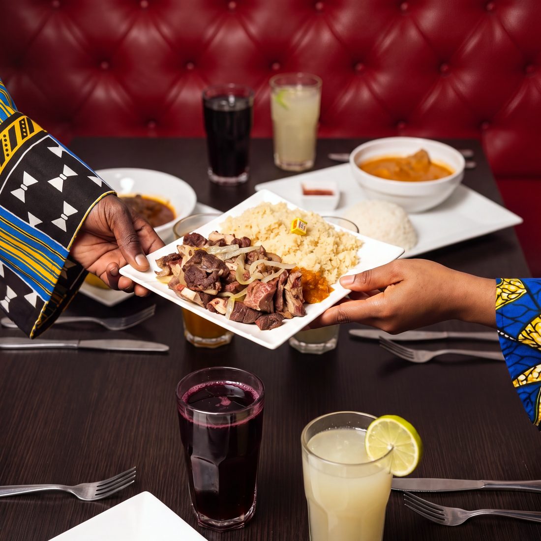 Photo d'une assiette de choukouya et attiéké qui passe de main en main entre amis, jus de bissap et de gingembre, banquette rouge, repas de groupe au restaurant africain Sepela, Lyon 7